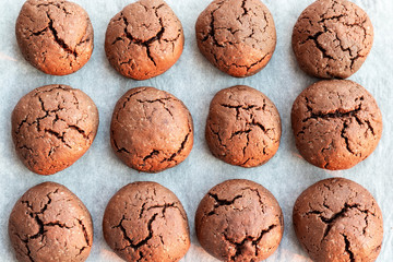 Baked cracked round chocolate cookies on a baking sheet with parchment paper just taken out of the oven. Tea or coffee snack. Closeup top view