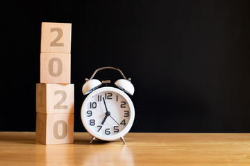 Alarm clock and wooden cubes with 2020 on wooden table. Concept for success in the future goal. Happy new year