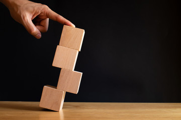 Finger pushing wooden cube on black background. Investement Risk management concept