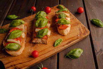 toast bread with mozzarella basil and cherry tomatoes on wooden background