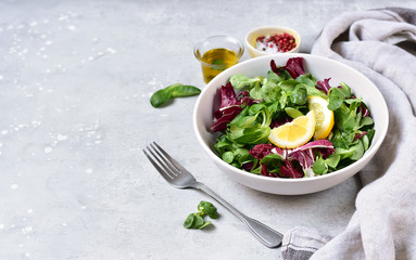 home delivery of dietary food  salad from radicchio, arugula, valerian leaves with lemon and olive oil in a white bowl on a gray background. vitamin diet salad recipe. selective focus, copy space