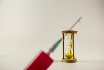 A blurry image of a syringe on an hourglass background, as a symbol that everything is of course.