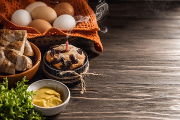 Easter table with Easter cake, homemade sausage. Homemade eggs, herbs and mustard.
Happy Easter. Dark wooden background. Copy space, place for text.