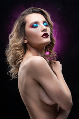 Beautiful topless busty girl with blue makeup poses on black and pink background, covering her breast with her hands. Fashionable, advertising and commercial portrait design.