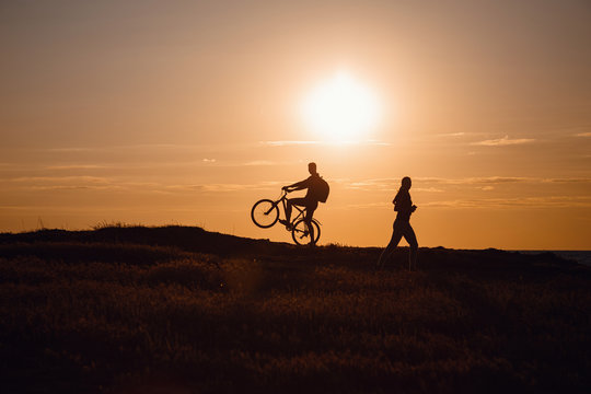 silhouette of men on a bicycle and a woman running towards him against a sunset