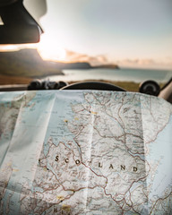 Planning a Road Trip adventure around Scotland with a map in hands parked overlooking the sunset