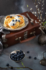 Cottage cheese pancakes, syrniki, curd fritters with fresh blueberries and sour cream on dark vintage background. Side view. Cookbook recipe. Russian breakfast menu