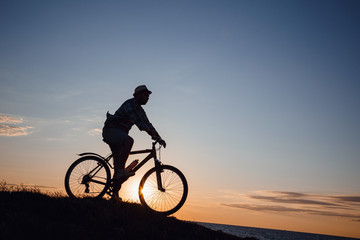 silhouette of a hipster man on a bicycle on sunset background