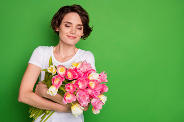 Photo of beautiful cute lady wavy short hairdo hold big tulips surprise bunch present secret admirer eyes closed overjoyed wear casual white t-shirt isolated green color background