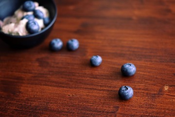 Closeup of ice cream with blueberries in black bow. Some blueberries spilled out on wooden table. Shallow DOF, horizontal.