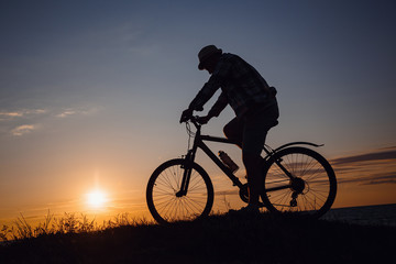 silhouette of a hipster man on a bicycle on sunset background