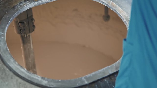 Toothpaste production process.  A worker opens a large steel production container with toothpaste.