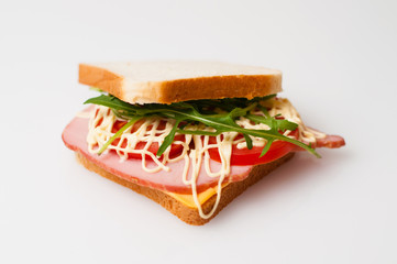 Sandwich made of bread for toast, balyk, tomatoes, arugula, cheese and mayonnaise on white plate side view