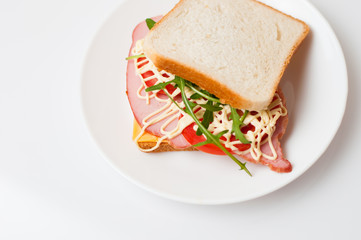 Tasty sandwich with ham or balyk, tomato, arugula, cheese, mayonnaise and white bread for toast on a plate on a white background view from the top flat lay, copy space