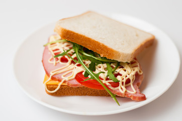 Tasty sandwich with ham or balyk, tomato, arugula, cheese, mayonnaise and white bread for toast on a plate on a white background