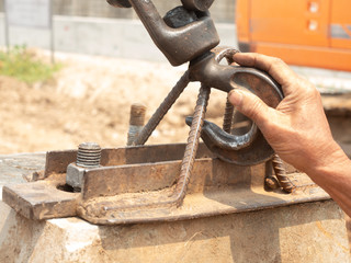The right hand of the worker is holding the hook to fasten on the bracket for lifting the material to move with the crane.
