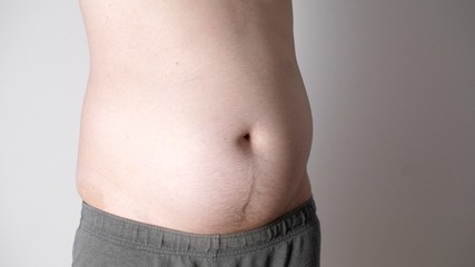 Naklejka premium Fat male stomach. Weight loss or weight gain during quarantine. Attractive man with tattoos with obese bare belly. Close-up of male beer belly of sexy man. Bodypositive