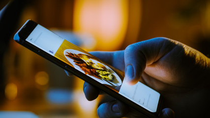 Close-up Macro: Person Holding and Using Smartphone, Browsing through Pictures on Social Network...