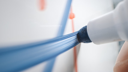 Macro Shot of a Blue Marker Pen Being Held with a Hand. Person Drawing a Blue Line on a Whiteboard.