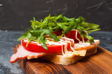 Appetizing sandwich with ham or balyk, arugula, cheese, tomatoes and mayonnaise on a cutting board side view