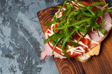 Appetizing sandwich with ham or balyk, arugula, cheese, tomatoes and mayonnaise on a cutting board top view flat lay