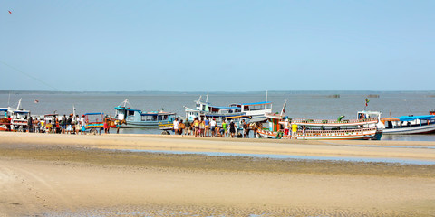 Fototapeta na wymiar Panorama de margem de rio com chegada de barcos na areia e turistas esperando para embarcar.