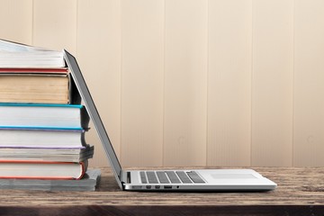 Stack of books with modern laptop on table