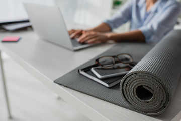 selective focus of businesswoman working on laptop at workplace with fitness mat, notepad,...