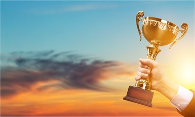 Hand holding golden trophy on the sky background