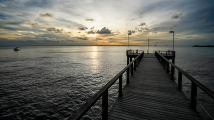 Fototapeta na wymiar Pier de madeira em direção ao mar no pôr-do-sol com lancha isolada distante.