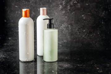 Three white cosmetic cream bottles with shampoo, shower gel and body balm, care. Copyspace on a black stone background