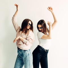 Two young girls in sunglasses have fun and dance on a white background