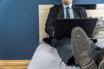 Home office concep with a man dressed in a suit in bed with a laptop