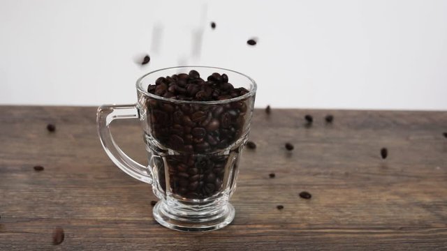 coffe beans falling into a glas on a wooden table with white backround in slow motion