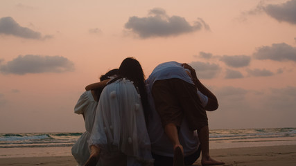Asian young happy family enjoy vacation on beach in evening. Dad, mom and kid sit, hug relax together near sea when looking silhouette sunset. Lifestyle travel holiday vacation summer concept.