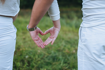 A woman and a man in white suits show with their hands, fingers a heart on nature. Photography, concept.