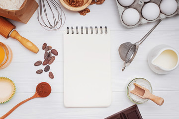 Ingredients and utensils for bakery or making dessets and blank paper notepad on the white table.