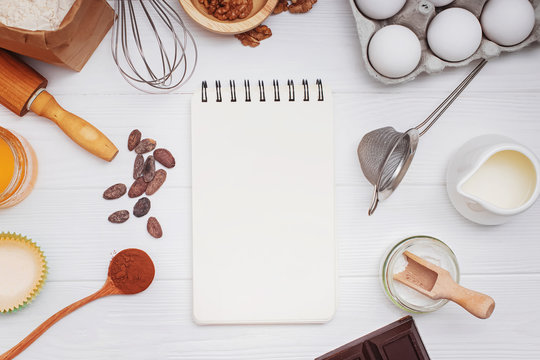 Ingredients and utensils for bakery or making dessets and blank paper notepad on the white table.