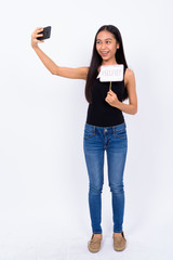 Full body shot of happy young Asian woman taking selfie