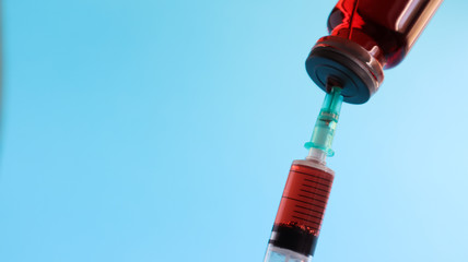 Coronavirus flu and pandemic vaccines, syringe and vial with red liquid on a blue background. medical concept, subcutaneous injection, treatment of the disease. Copy space for text or logo