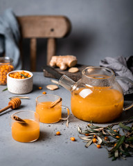 Sea buckthorn tea in a glass teapot. Leaves and berries are scattered on the table.