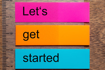 Three bookmark stickers with the words let’s get started, on a dark natural wooden table