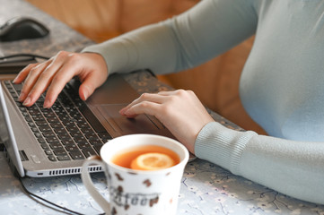 Obraz na płótnie Canvas woman's hands on a computer keyboard next to tea with a lemon theme of remote work in a pandemic
