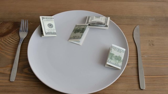 Dollars are falling in a plate close-up. Concept: food expenses, overeating, dietary expenses, earnings, cooking, restaurateur