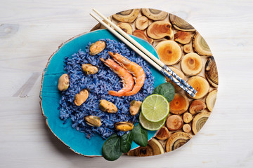 Blue rice with shrimp, mussels, lime and basil leaves on a blue plate. Seafood