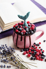 Chocolate dessert with black and red currants in a pink cup on a white background. Near the lavender flowers. In the background a book