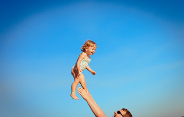 happy little girl in a swimsuit flies in the sky, dad throws up his daughter and catches her. Background of blue sky. Sea, vacation and travel. Father's day. Daughter's day. Family day.