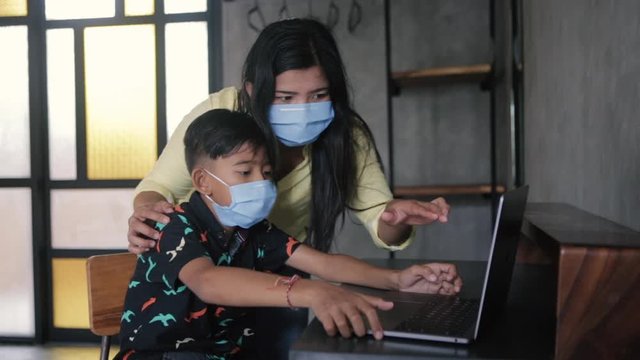 Lockdown and school closures. Mother helping her child with face mask studying online classes at home. Quarantine, self-isolation, online education concept, home schooler during COVID-19 pandemic