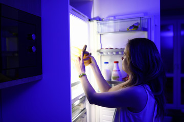 Fototapeta na wymiar Woman at night opened refrigerator and takes out food portrait