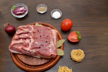 a piece of raw pork and vegetables and spices in the kitchen on a wooden table cooking ingredients 